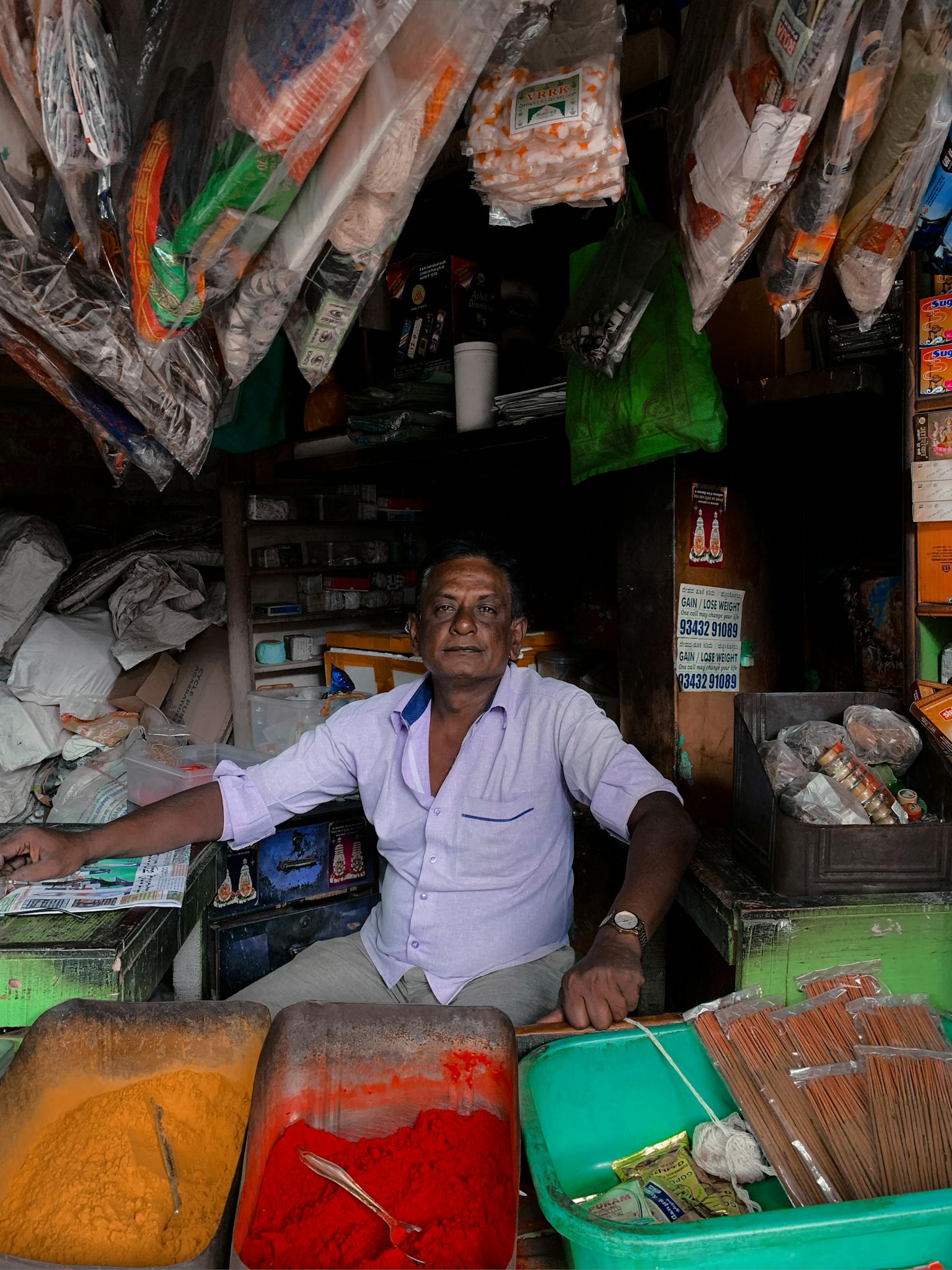 Vendor in an Indian market stall with vibrant spices and goods on display.